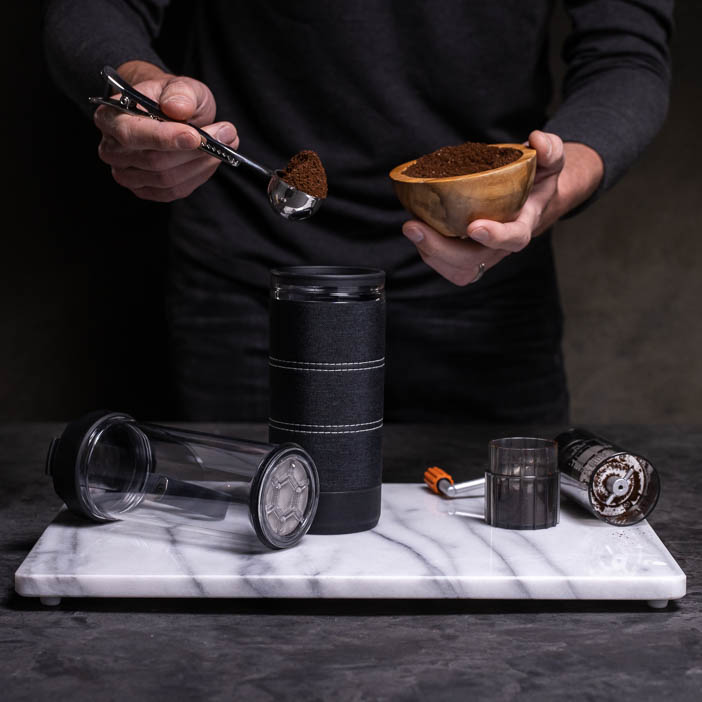 Man scooping coffee grounds into tumbler for a great men's drink gift.