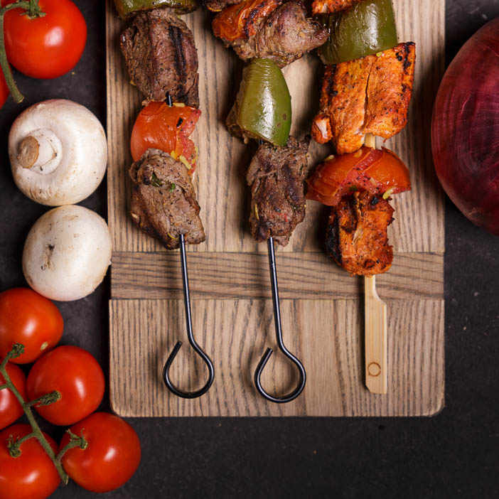 Two metal and one meat skewer on a cutting board for a great men's grilling gift.